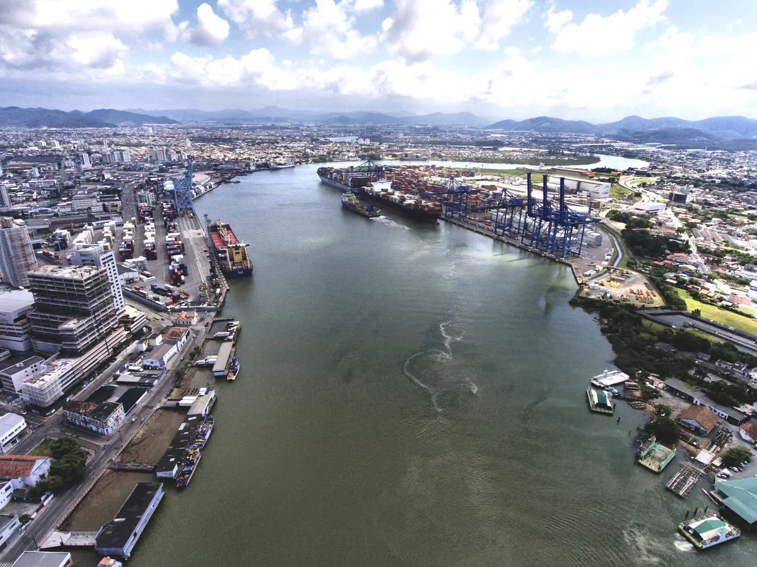 Vista aérea de um rio urbano com o complexo portuário e a cidade nas duas margens